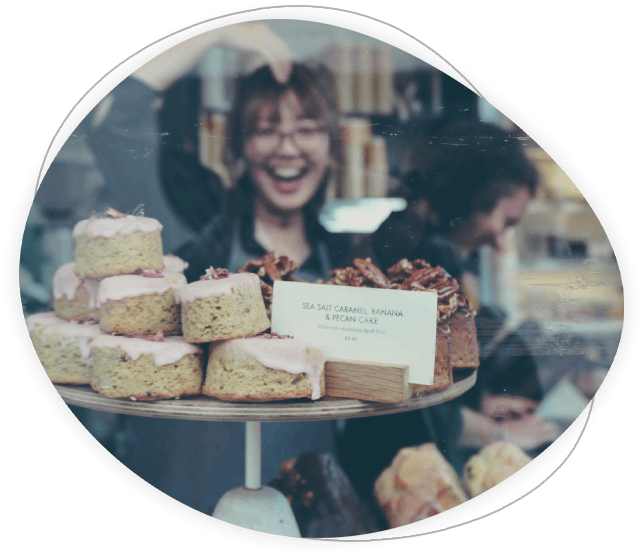 El equipo de panadería sonríe y sostiene pasteles dentro de la tienda.